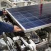 A man holds a solar panel as it comes off a production line in a factory