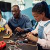 A Black man and two children work on an electrical engineering project