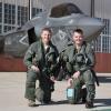 Hamilton and Frey kneel in front of a fighter jet in full flight gear.