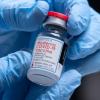 Gloved hands holding a dose of the Moderna COVID-19 vaccine. 