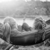 A black-and-white photo of two girls sitting next to one another, on a hammock, faces away from the viewer