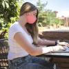 Female student wearing mask working at laptop outside