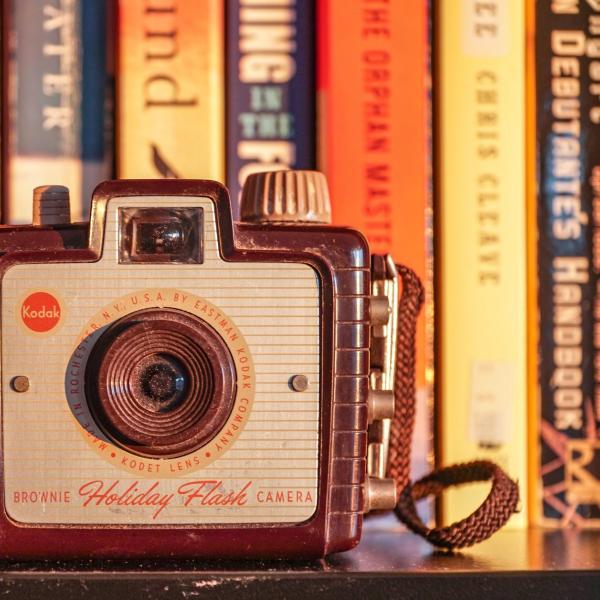 GREY CAMERA AGAINST BOOKS BACKDROP