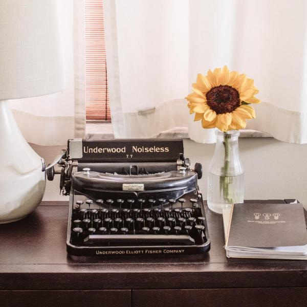 A typewriter on a desk next to flowers