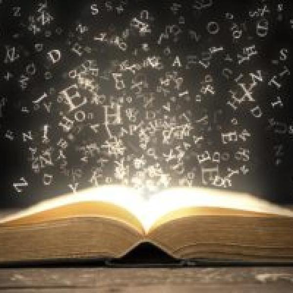 Letters floating out of an open, illuminated book on a table