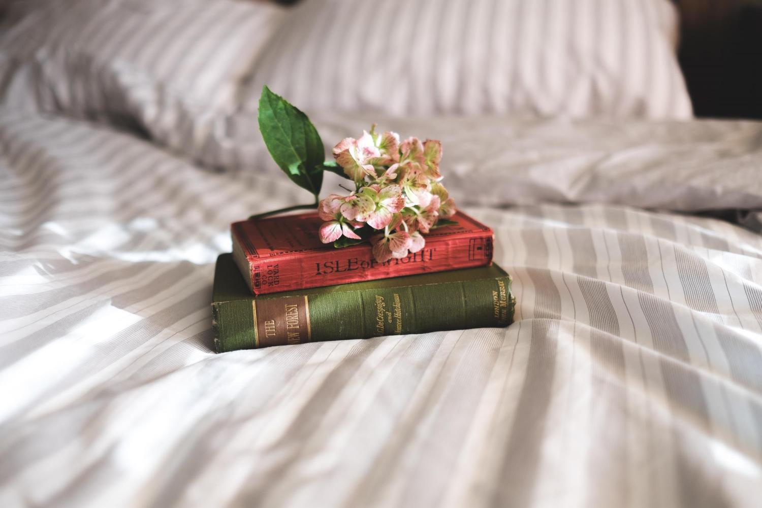 a pile of books on a bed topped by flowers