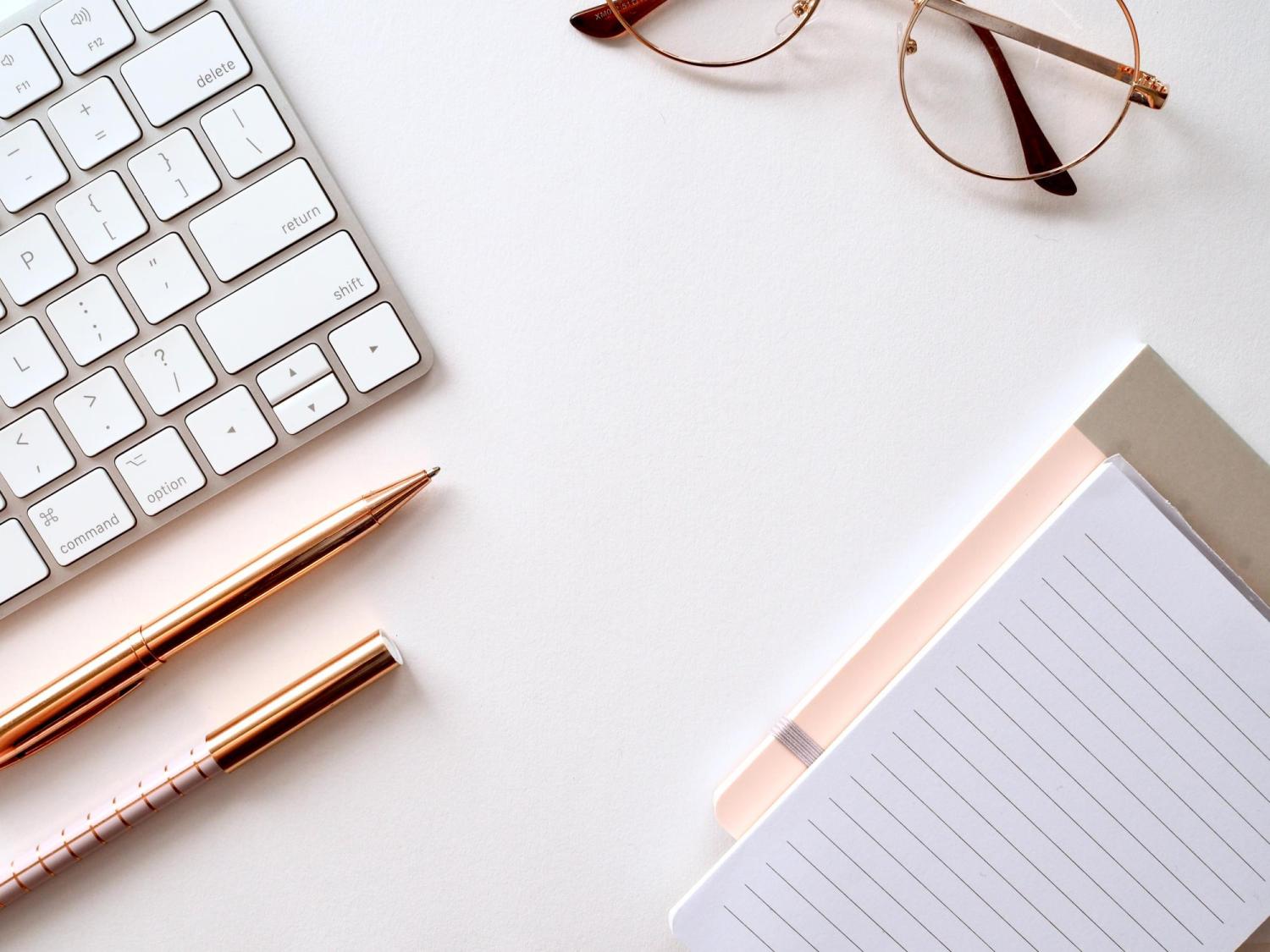 A white desk with a keyboard and a pair of glasses