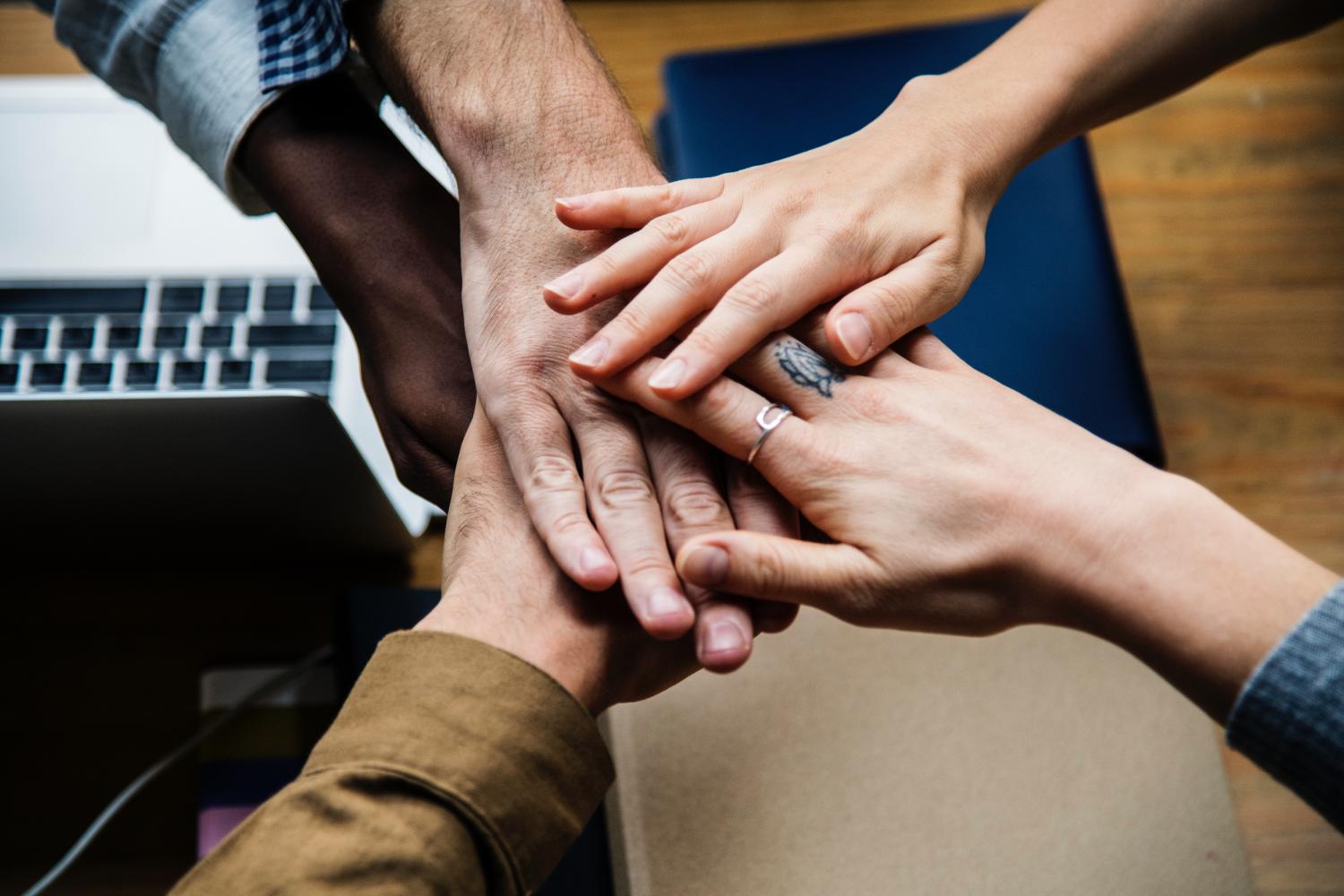 A group of people with their hands all touching showing support and camaraderie.