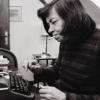A woman is sitting at a desk in front of a typewriter