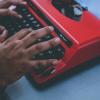 A person typing on a red typewriter
