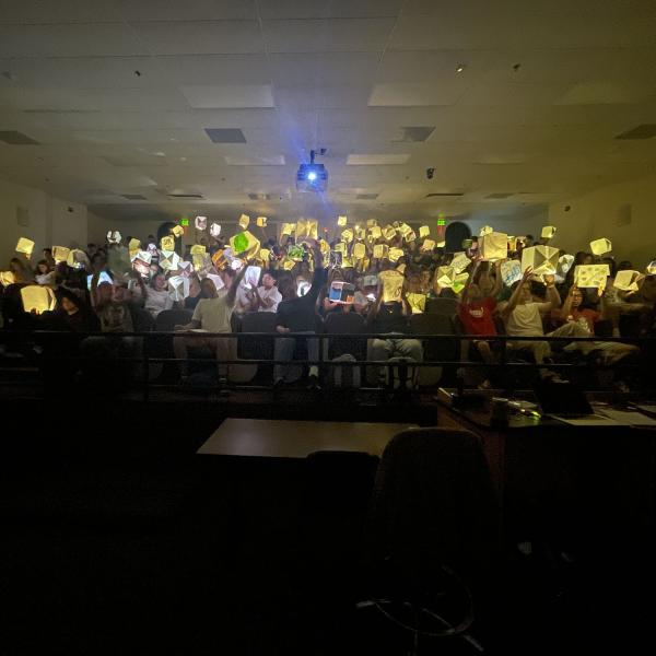 Students gathered in a dark classroom hold lit up paper cubes