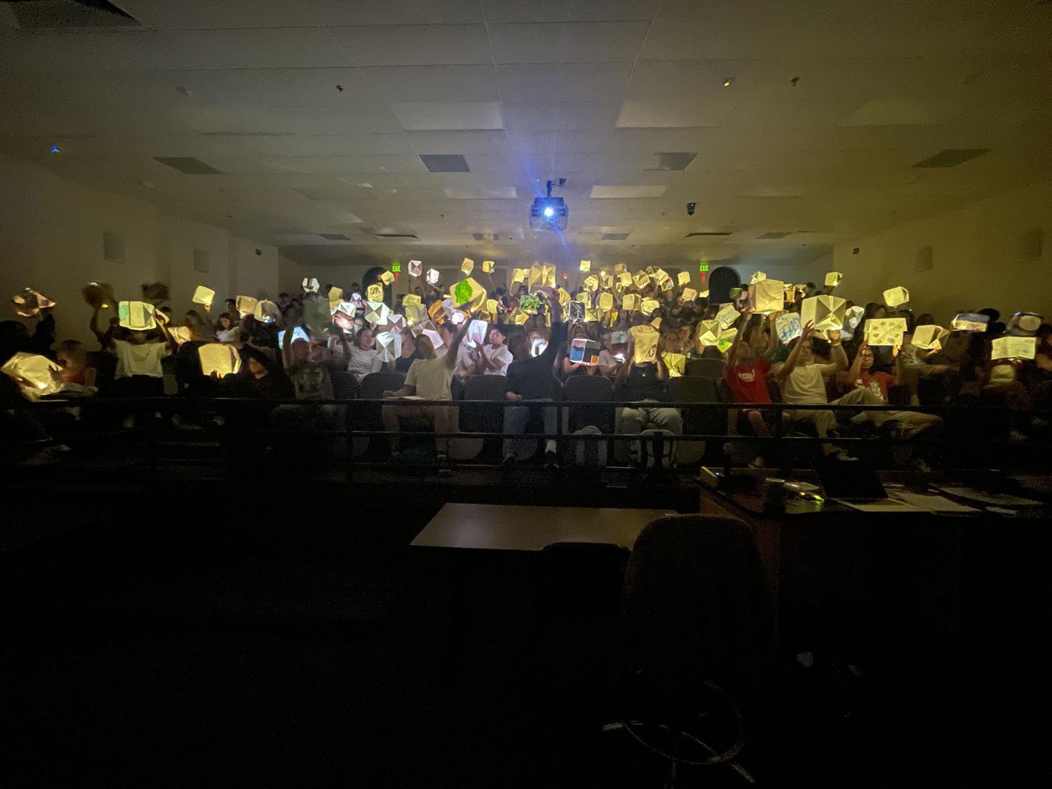 Students gathered in a dark classroom hold lit up paper cubes