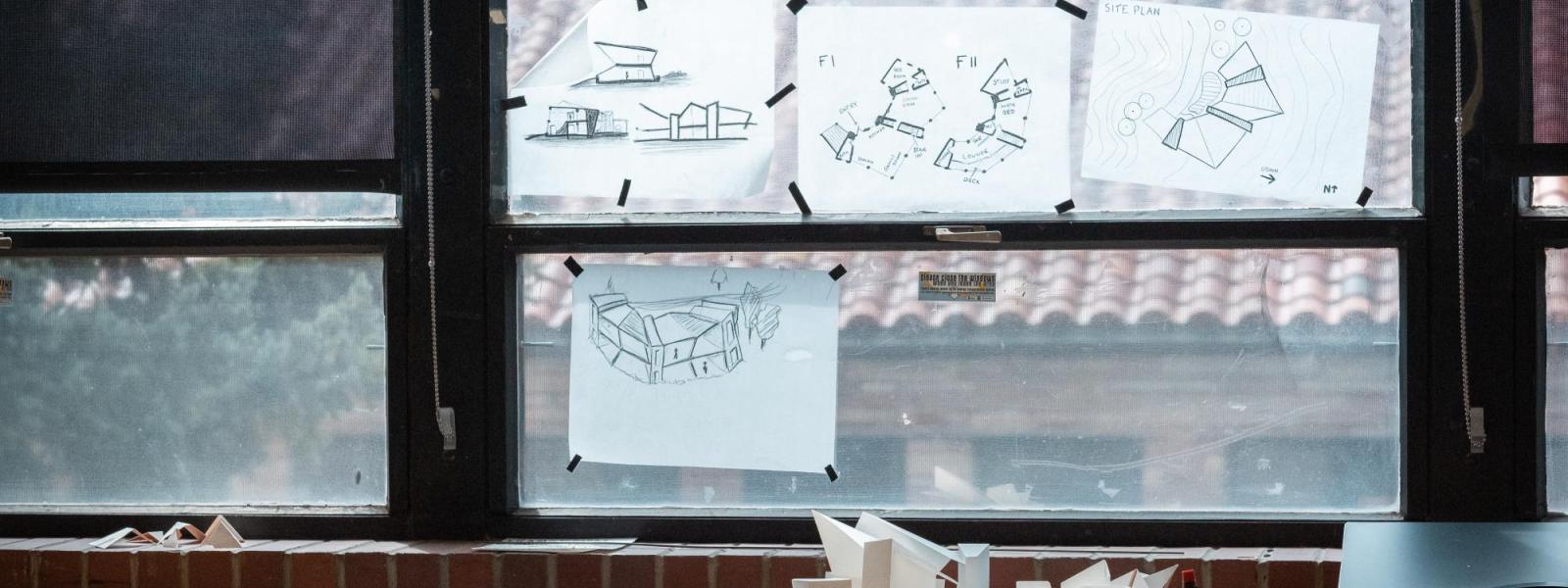Trace paper draft drawings hang on window for easy viewing.