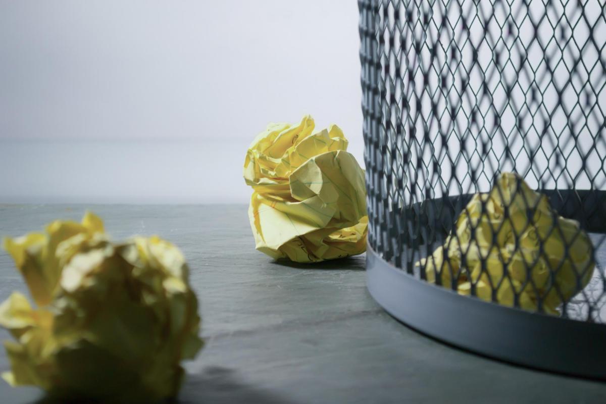 Image of crumpled yellow paper on the floor next to a waste bin