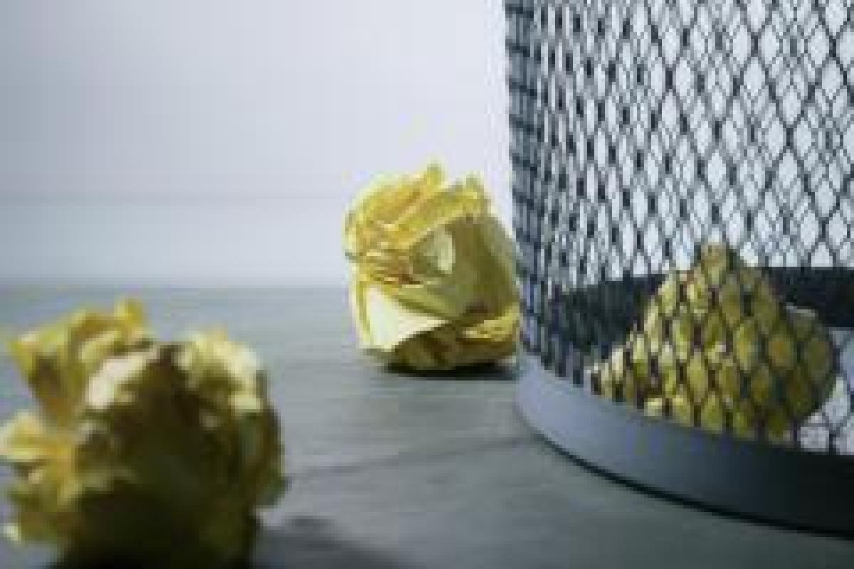 Image of crumpled yellow paper on the floor next to a waste bin