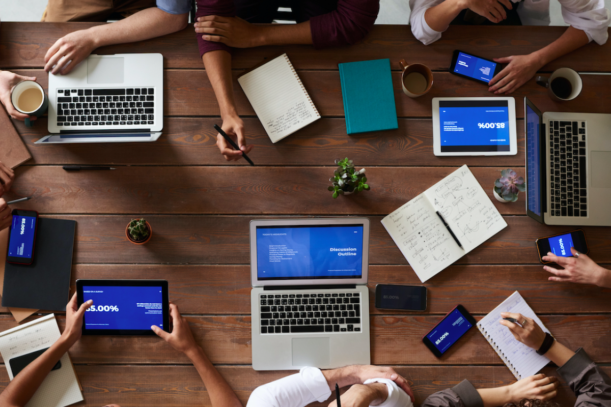 Aerial view of eight people sitting at a table with computers and other office items