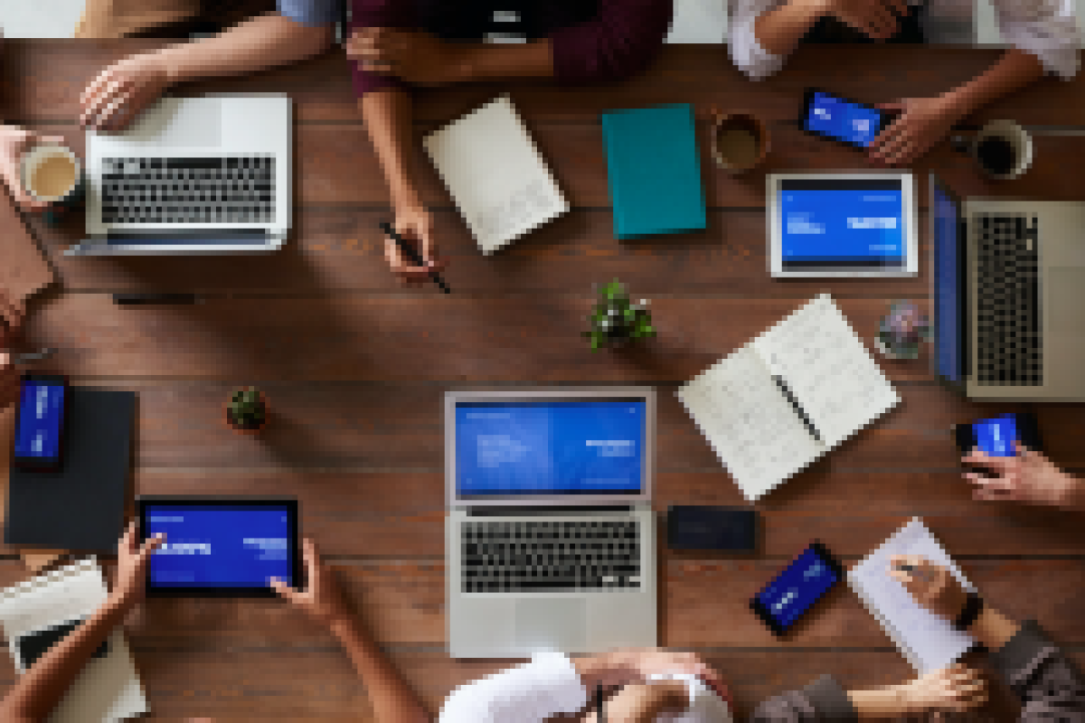 Aerial view of eight people sitting at a table with computers and other office items