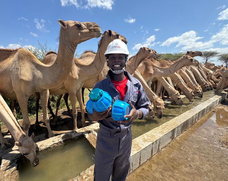 A man holding two water bottles with camels in the background.