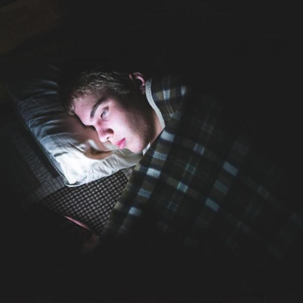 Person lying in bed in the dark looking at phone