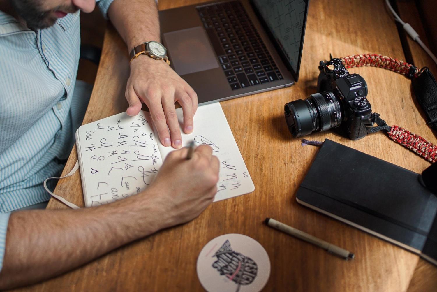 Person sketching designs in notebook with DSLR camera nearby
