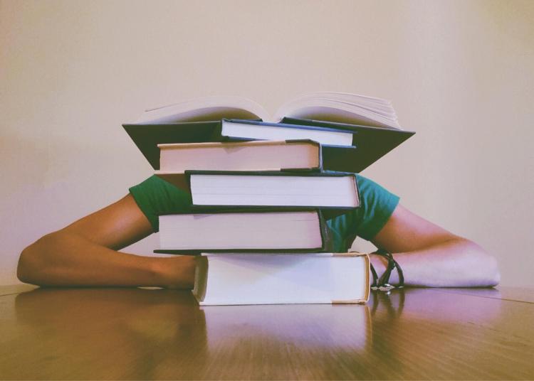 Student buries head behind pile of books