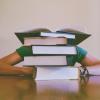 Student buries head behind pile of books