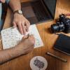 Person sketching designs in notebook with DSLR camera nearby