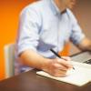Person writing in notebook at computer