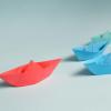 red paper boat leads a pack of blue and green paper boats