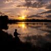 Person fishing in a lake at sunset.