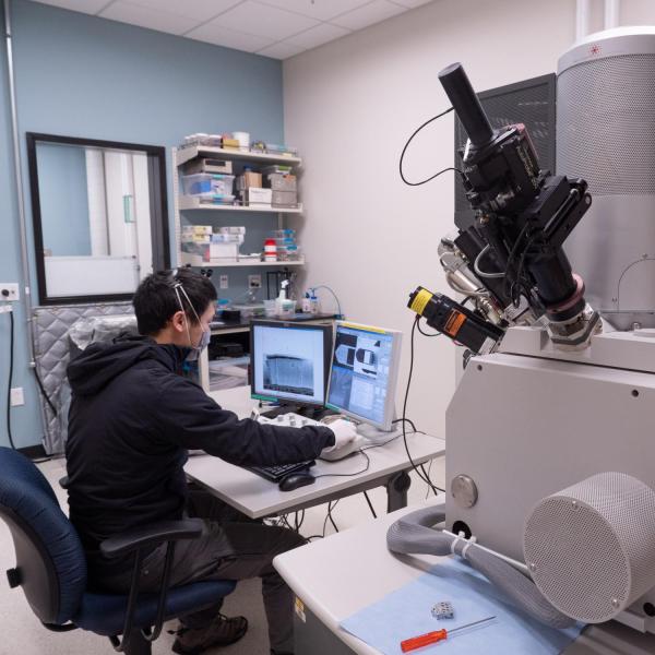 A close up of lab equipment with a person in the background working on a computer.