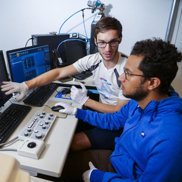 2 people are looking at a monitor. One person is gesturing at the screen.