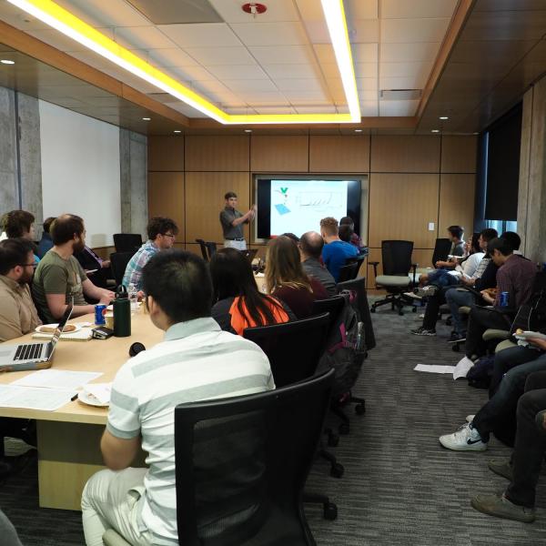 Students are sitting around a table watching a presentation