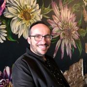 Photo of Adrian, a man in glasses with a beard behind a flower mural 