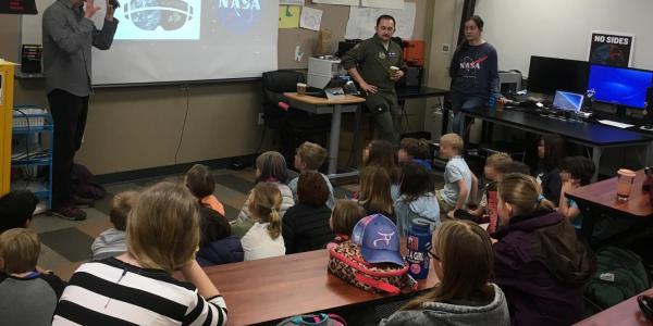 Students are watching a presentation about space. One of the presenters is generally gesturing towards the screen. 