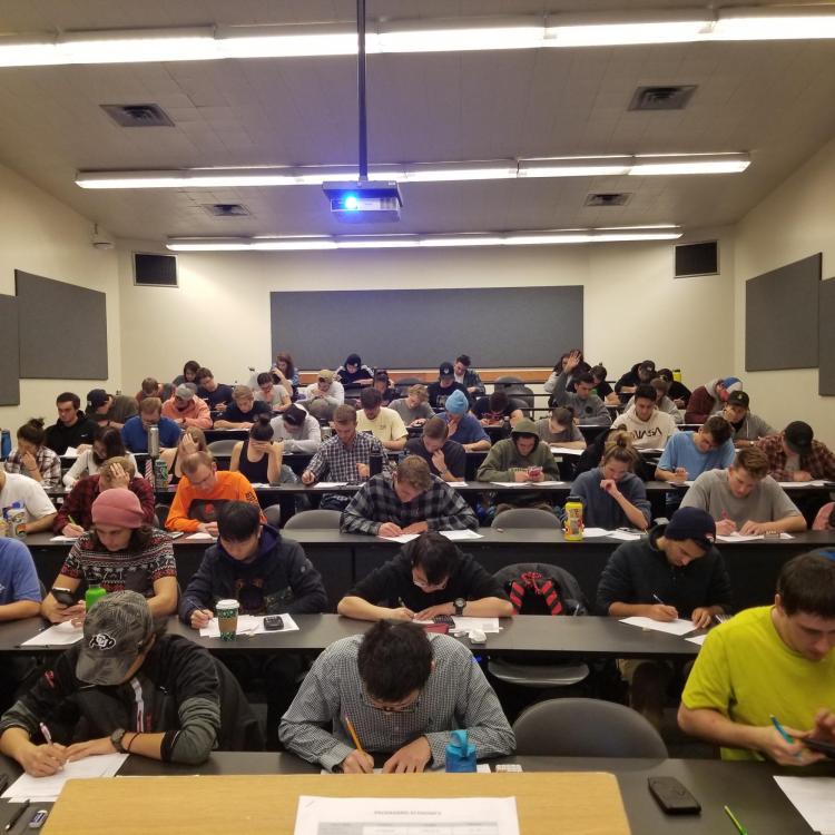 A classroom where students sit in rows of desks while writing on papers.