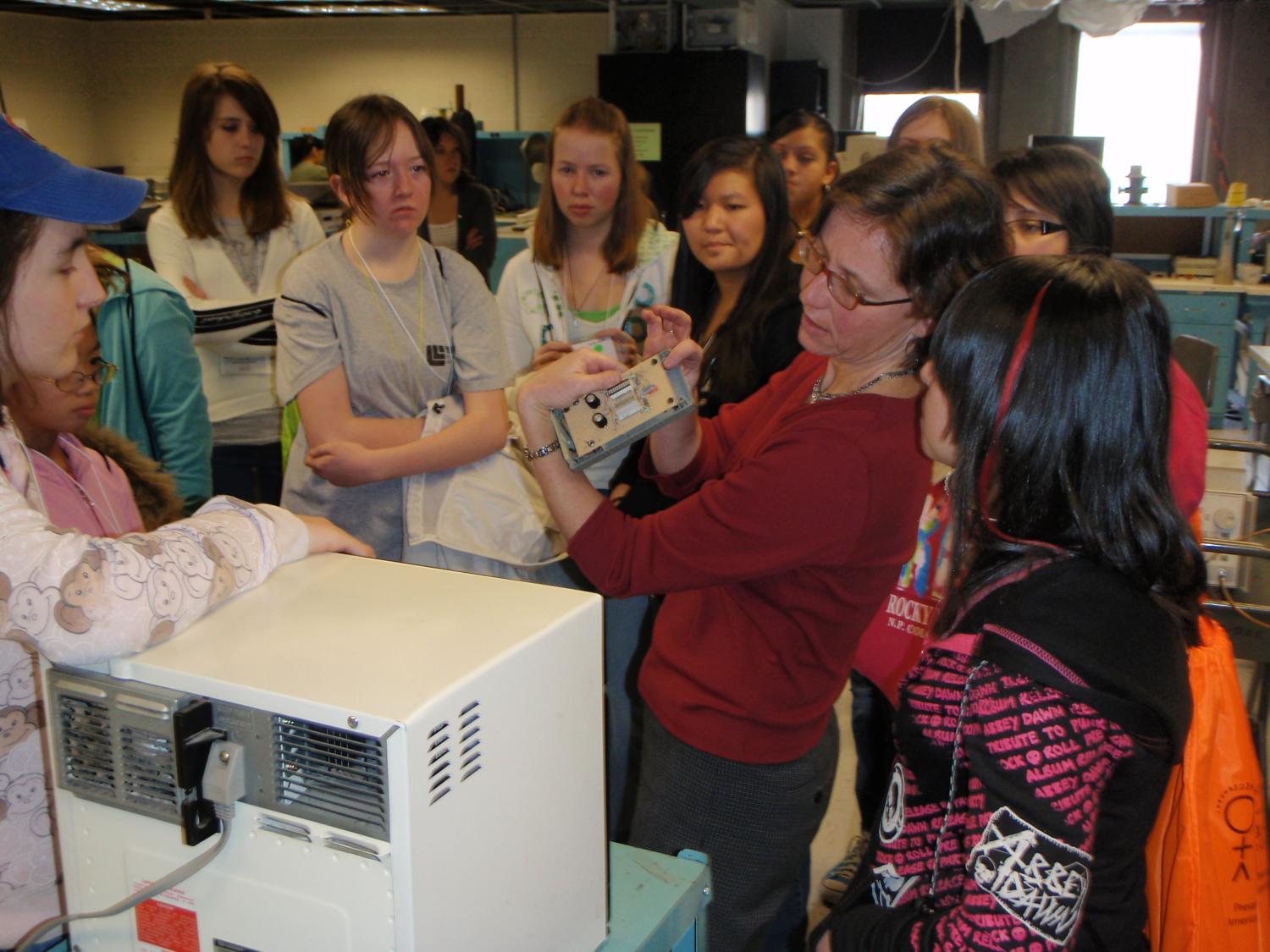 Zoya shows off a device in her lab to a group of high school women