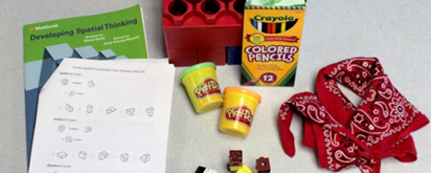 There are various items on a white background. There is a book titled Developing Spatial Thinking, a box of colored pencils, a red bandana, and play doh