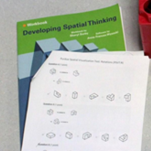 There are various items on a white background. There is a book titled Developing Spatial Thinking, a box of colored pencils, a red bandana, and play doh
