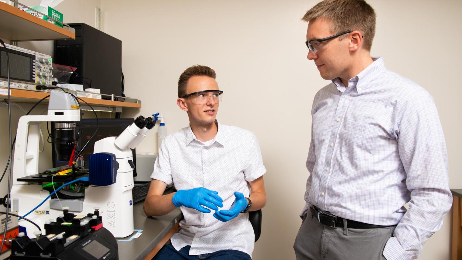 Two people talking in the lab by the microscope