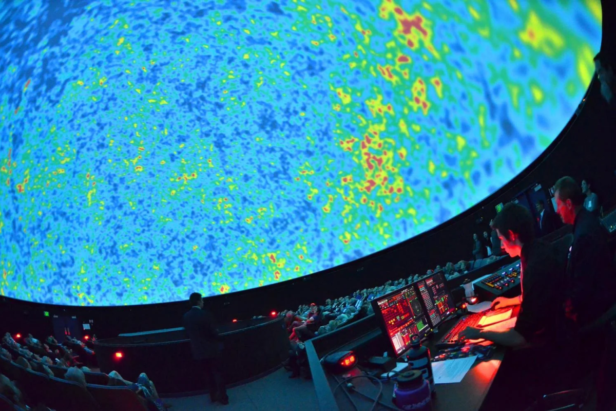 Interior of dome with colorful image of the cosmic microwave background in the screen, audience is seated and operator at console