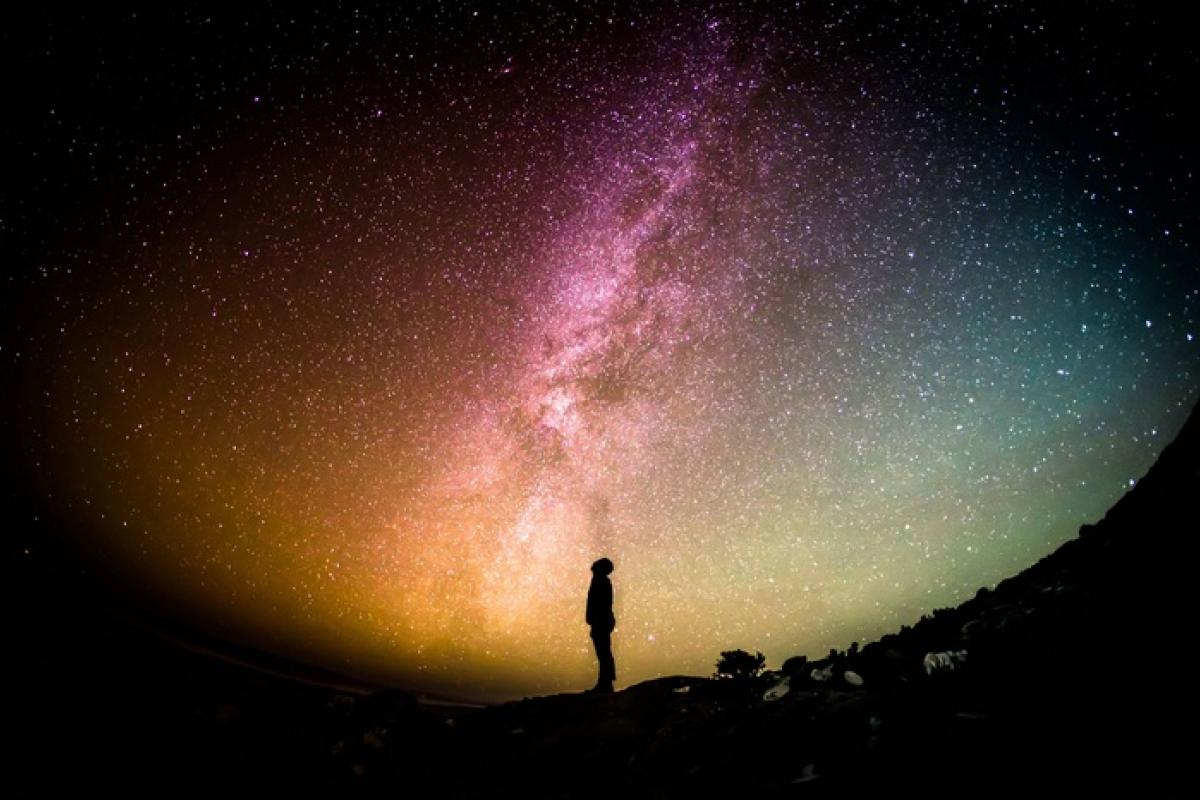Colorful photo of a person standing on a hill looking up at Milky Way galaxy copy