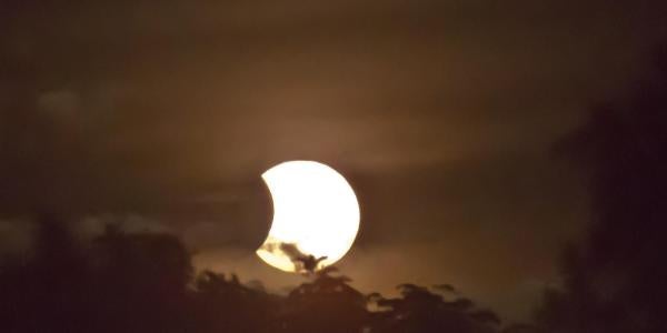 Photo of a total solar eclipse in progress clouds and trees in view