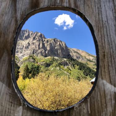 Photo taken through a wooden oval of the mountains and orange leaves from Gothic, Colorado