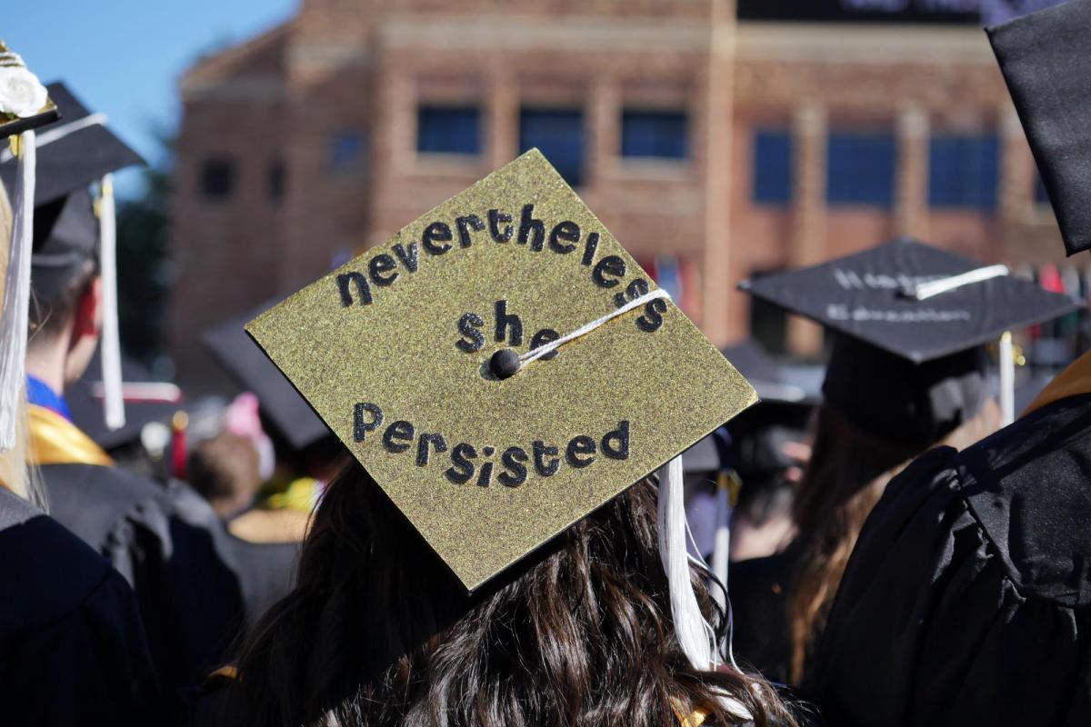 CU commencement student with mortarboard that says "but she persisted"