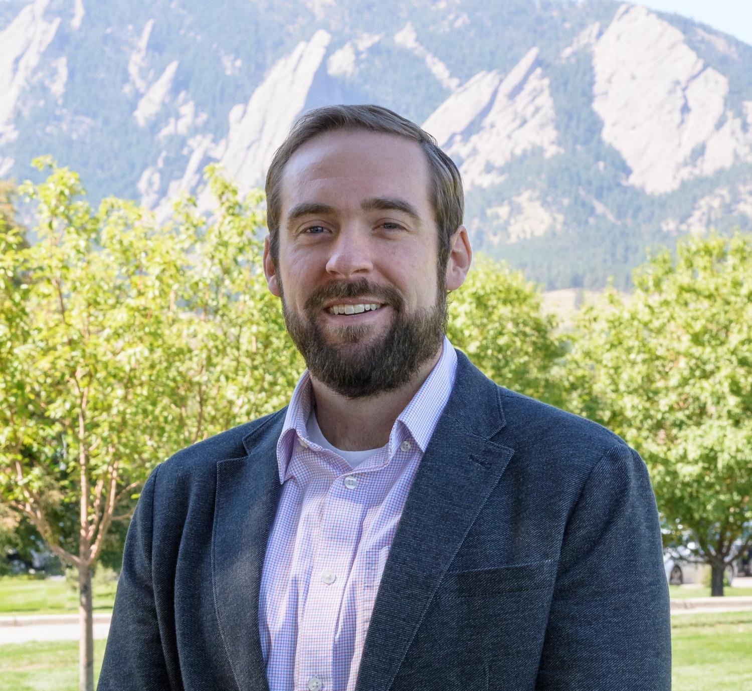 Brad Wham in a suit jacket and button down shirt in front of trees and the Flatirons
