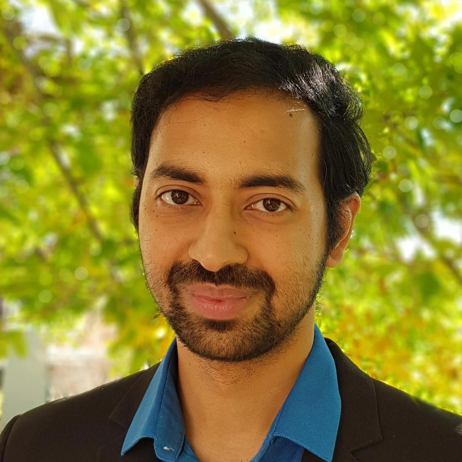 Srikanth S. C. Madabhushi in a button down shirt and jacket in front of tree branches,