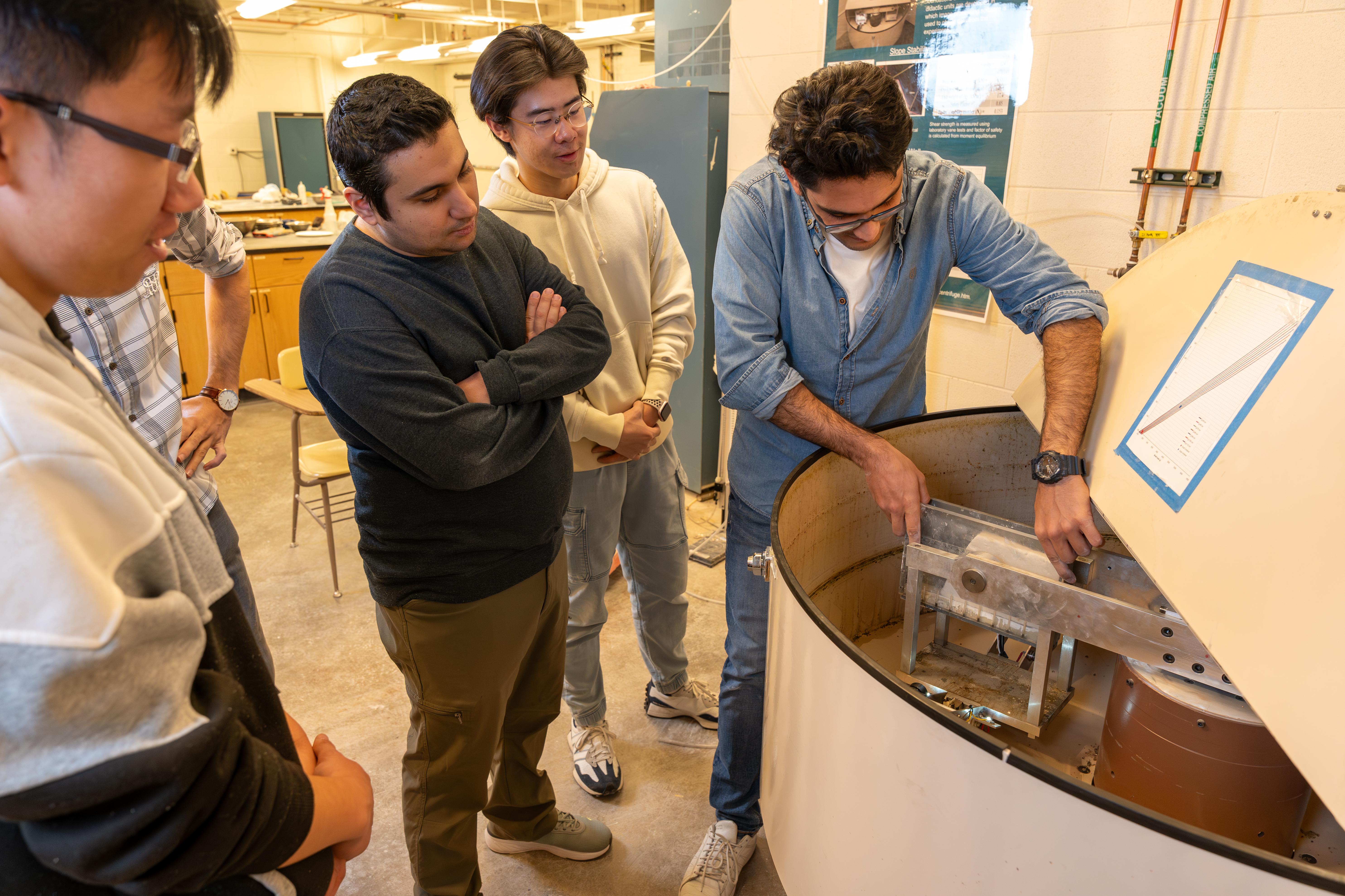 A demonstration of a small centrifuge in the geotech lab to three onlooking students.
