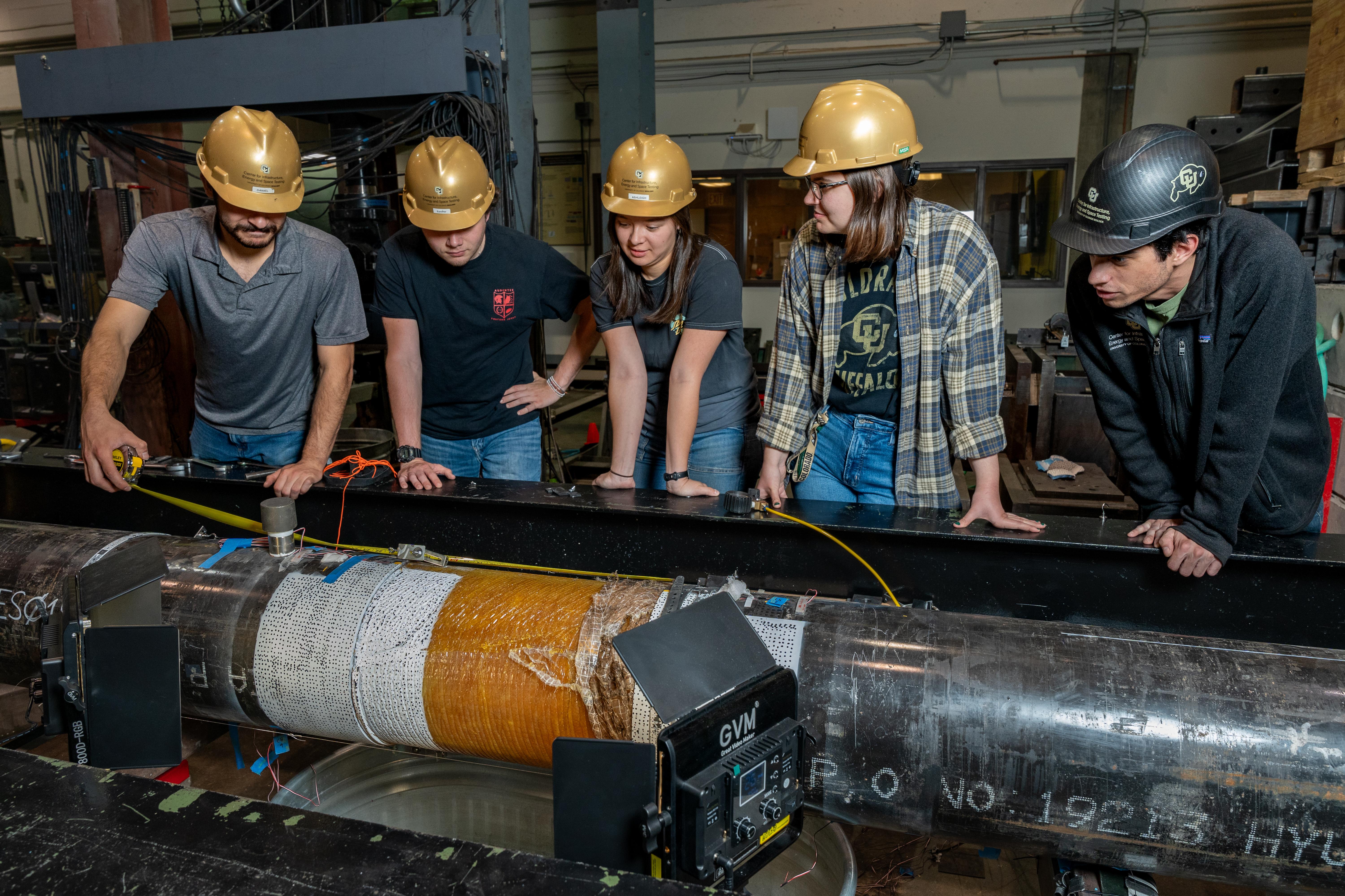 Researchers in the CIEST lab dressed in hard hats look over a large pipe that is being tested.