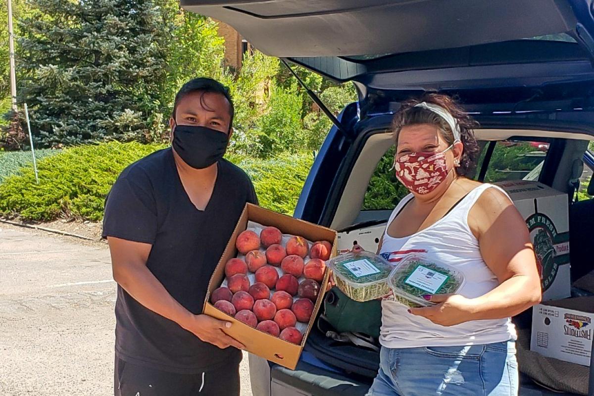 Man and woman holding boxes of fruit behind a car with it's trunk open